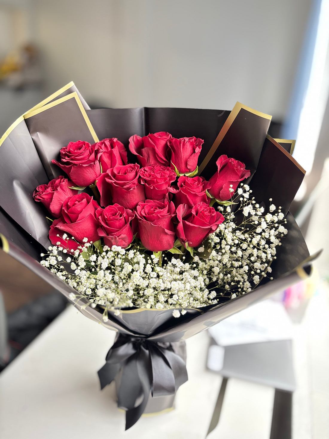 Bouquet of red roses with white flowers wrapped in black paper held by a person.