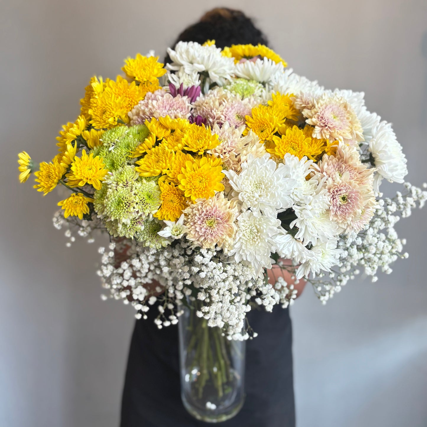 Person holding a large bouquet of flowers in front of their face against a neutral background