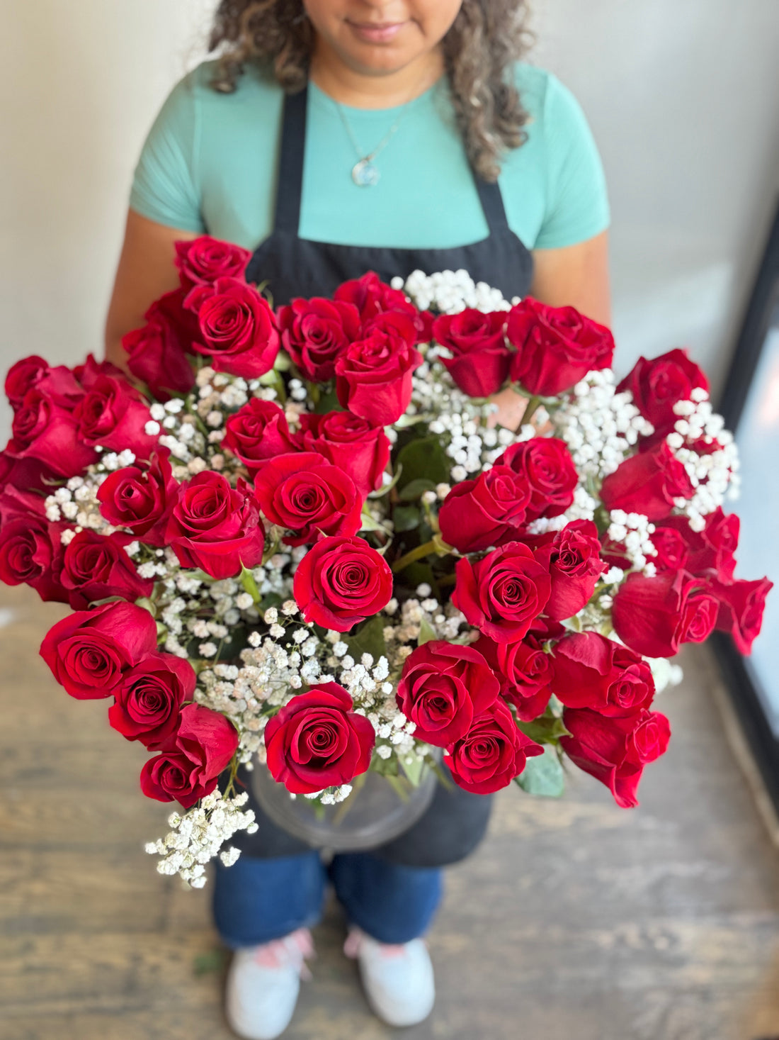 Person holding a heart-shaped arrangement of red roses and white flowers.