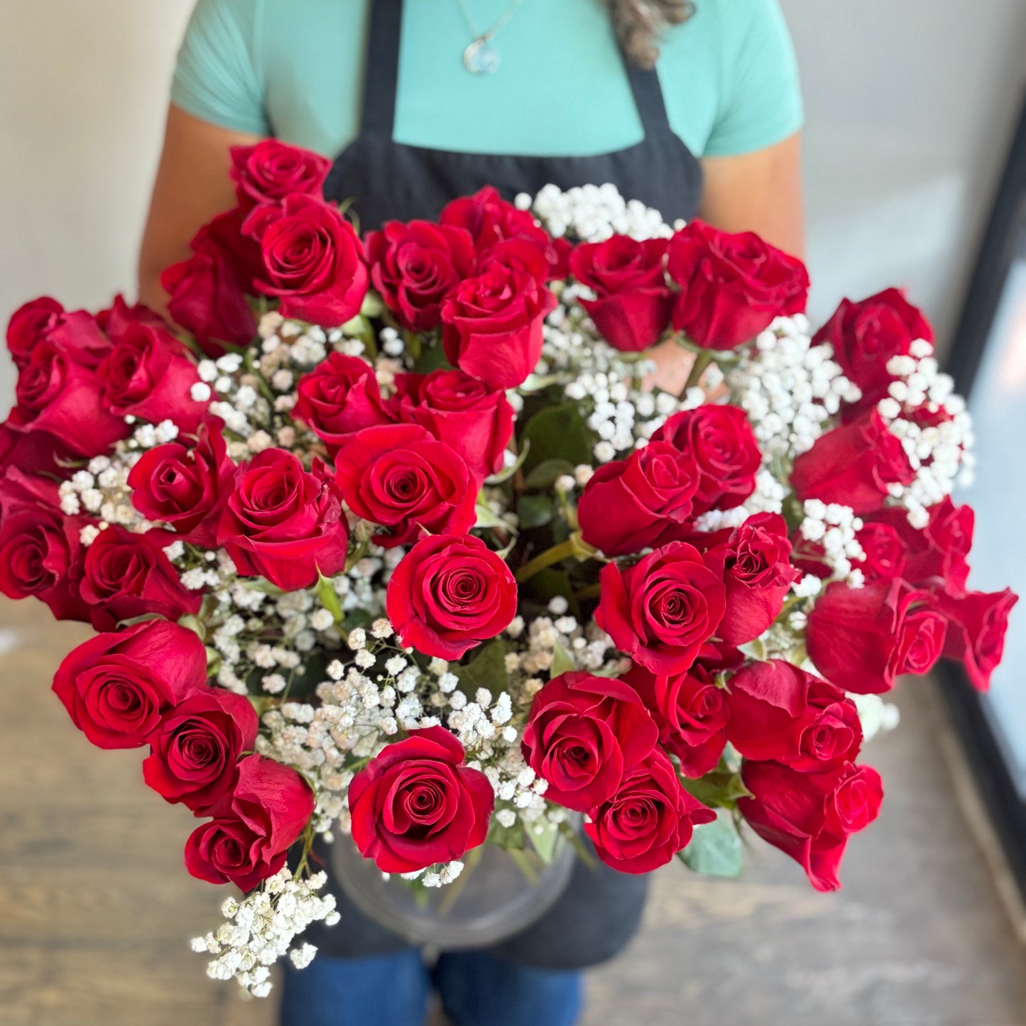 Person holding a heart-shaped arrangement of red roses and white flowers.