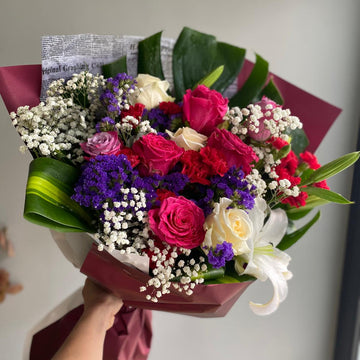 Bouquet of colorful flowers held by a person with a plain background
