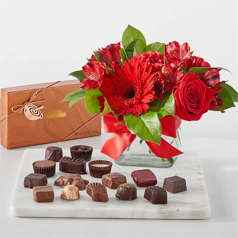 Vibrant red flower arrangement featuring bold red roses, carnations, and lush greenery, beautifully arranged in a decorative vase.
