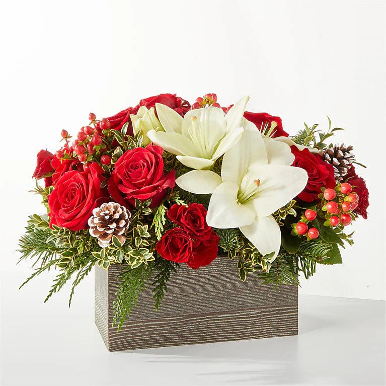 A festive Christmas flower basket featuring red roses, white lilies, red carnations, pinecones, and evergreens. The arrangement is designed in a rustic, decorative basket, perfect for holiday décor, gifts, or Christmas centerpieces