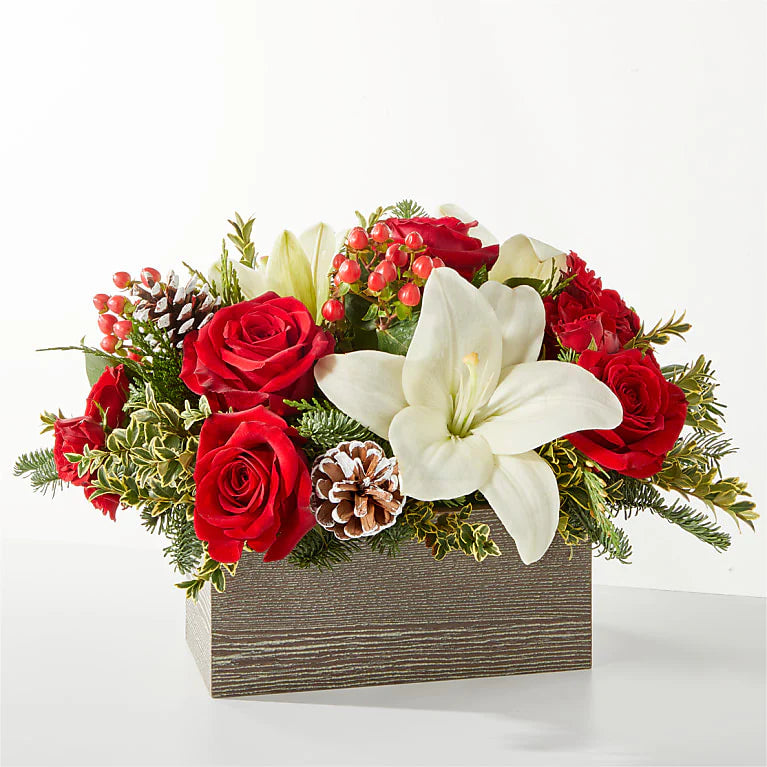 A festive Christmas flower basket featuring red roses, white lilies, red carnations, pinecones, and evergreens. The arrangement is designed in a rustic, decorative basket, perfect for holiday décor, gifts, or Christmas centerpieces
