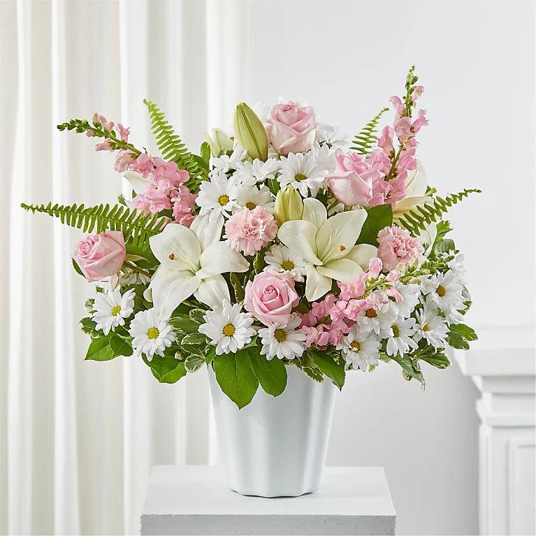 Bouquet of pink and white flowers in a white vase on a white surface with a white curtain background.
