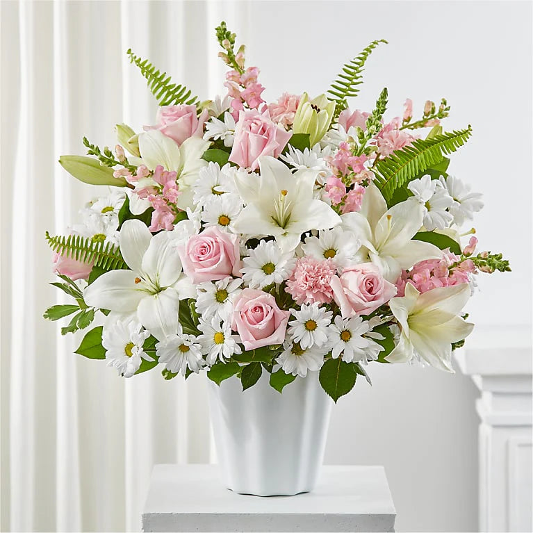 oft pink and white flower arrangement featuring roses, lilies, daisies, and carnations in a white tabletop basket, perfect for sympathy, new baby, or thoughtful gifting.