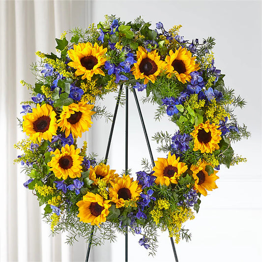 A handcrafted wreath featuring a lush base of vibrant sunflower greens, accented with clusters of deep purple statice flowers. The combination of fresh green foliage and the vivid purple blooms creates a striking, elegant contrast. The wreath is full and textured, offering a natural, cheerful look that is perfect for home decor or as a seasonal decoration.