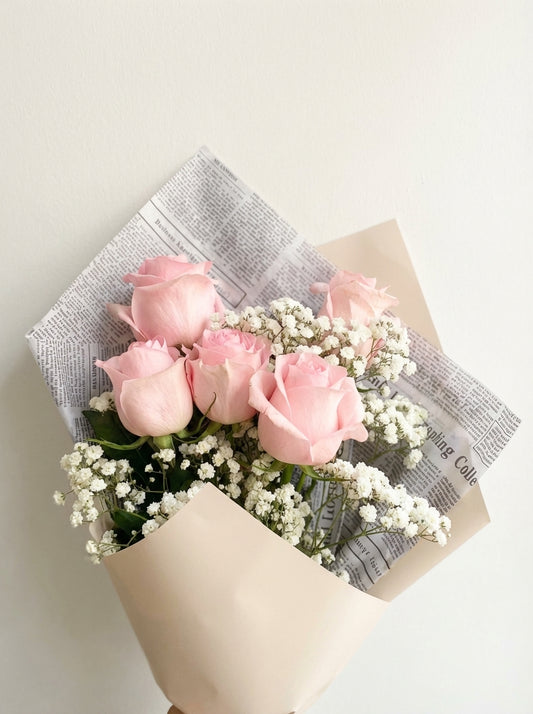 Bouquet of pink roses with baby's breath wrapped in newspaper on a light background