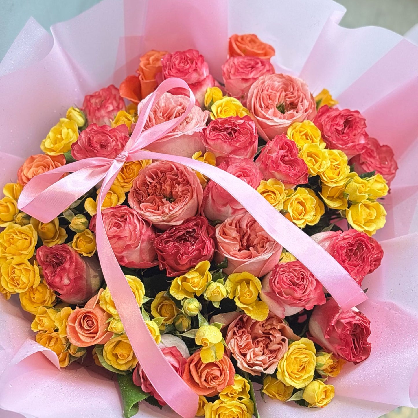 "A vibrant mixed bouquet featuring full-bloom pink roses and delicate yellow spray roses, creating a beautiful blend of soft pink and sunny yellow tones. The bouquet exudes a cheerful and elegant charm."