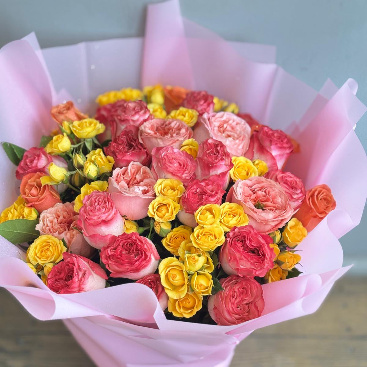 "A vibrant mixed bouquet featuring full-bloom pink roses and delicate yellow spray roses, creating a beautiful blend of soft pink and sunny yellow tones. The bouquet exudes a cheerful and elegant charm."