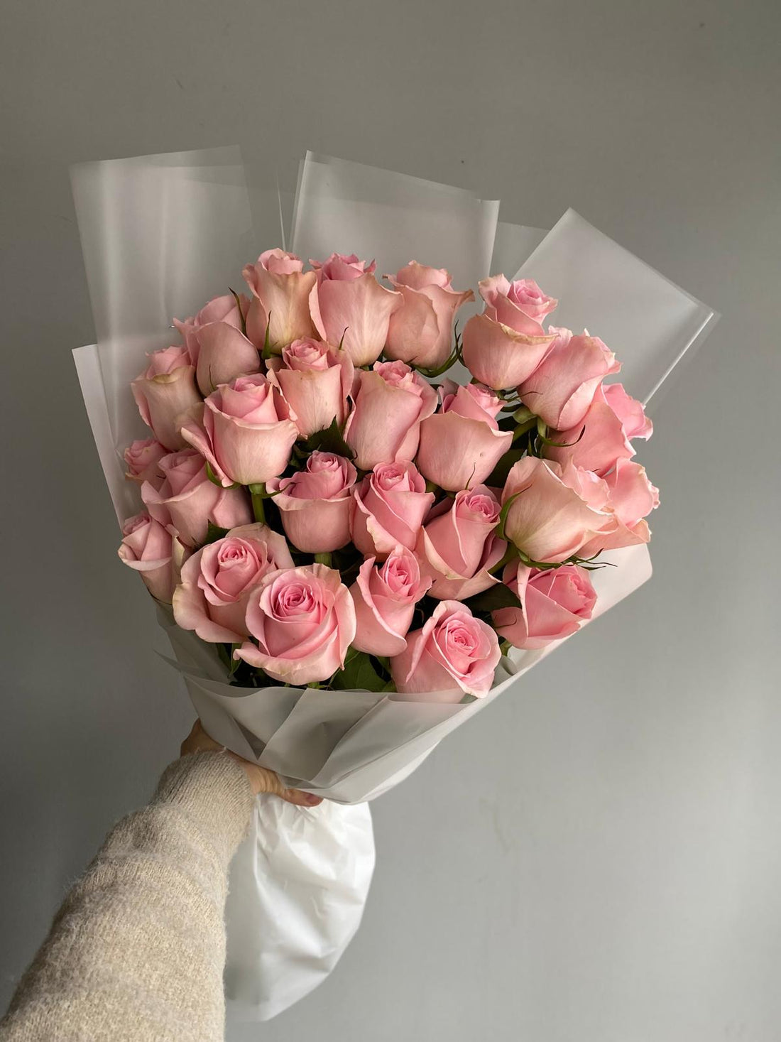 Bouquet of pink roses held by a hand against a gray background