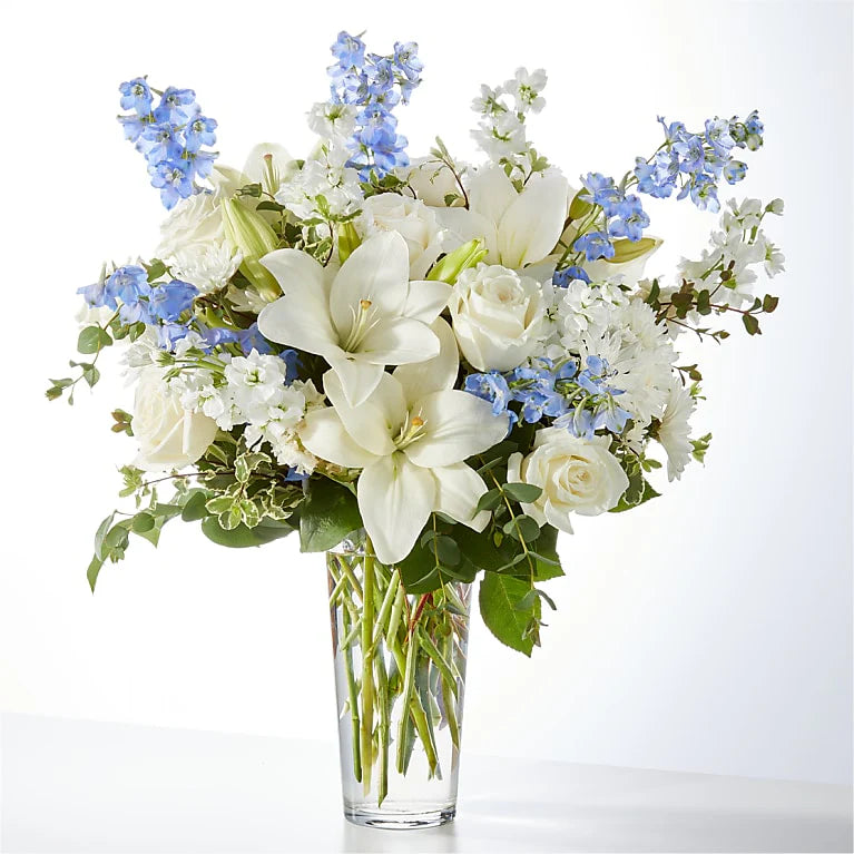 Bouquet of white lilies and blue flowers in a clear vase on a white background
