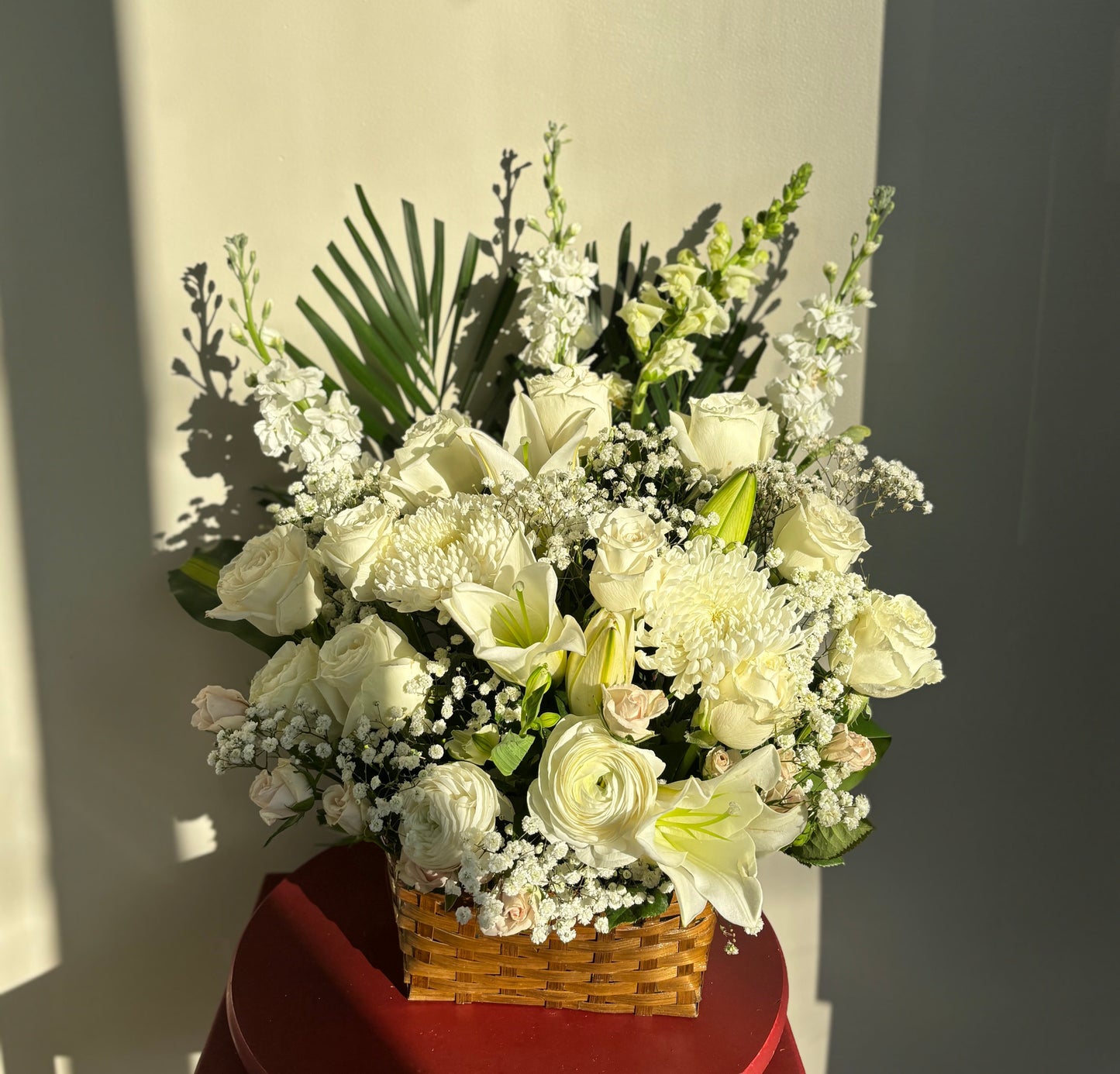 Bouquet of white flowers in a basket on a red stand against a plain background