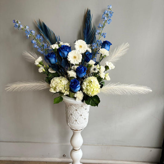 Floral arrangement with blue and white flowers in a decorative white vase on a wooden floor.