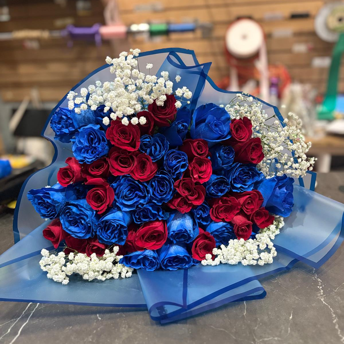 Bouquet of red, blue, and white roses on a gray surface with a blurred background.