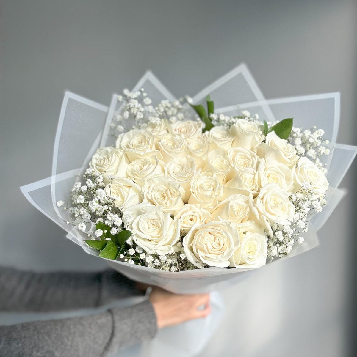 Bouquet of white roses held by a person against a gray background