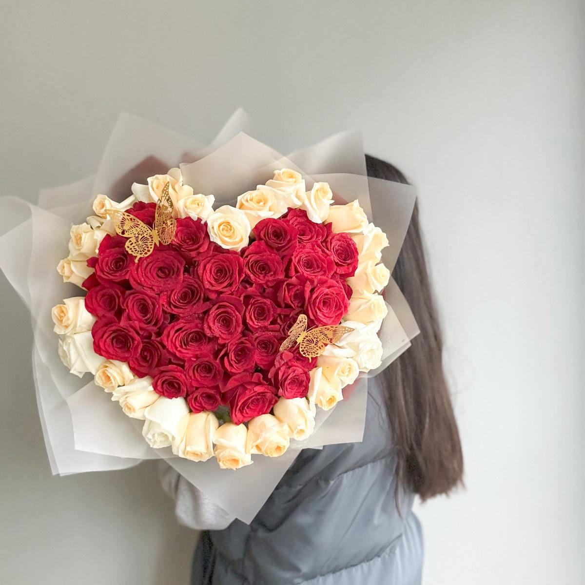 Heart-shaped bouquet of red and white roses held by a person against a plain background