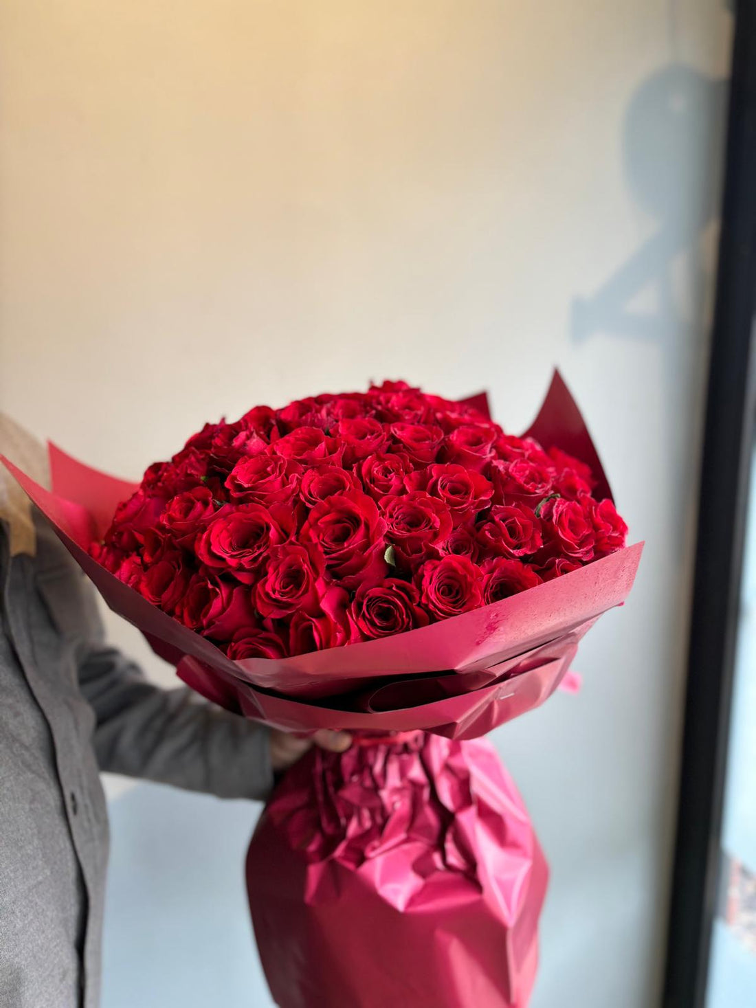 Bouquet of red roses wrapped in red paper against a neutral background