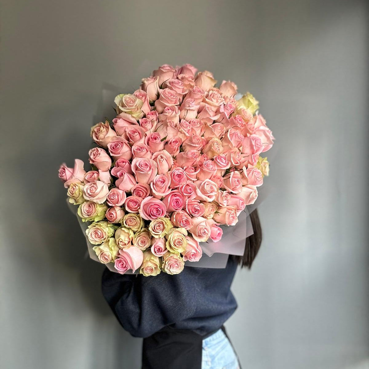 Person holding a large bouquet of pink and green roses against a plain background