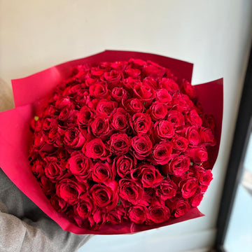 Bouquet of red roses wrapped in red paper against a neutral background