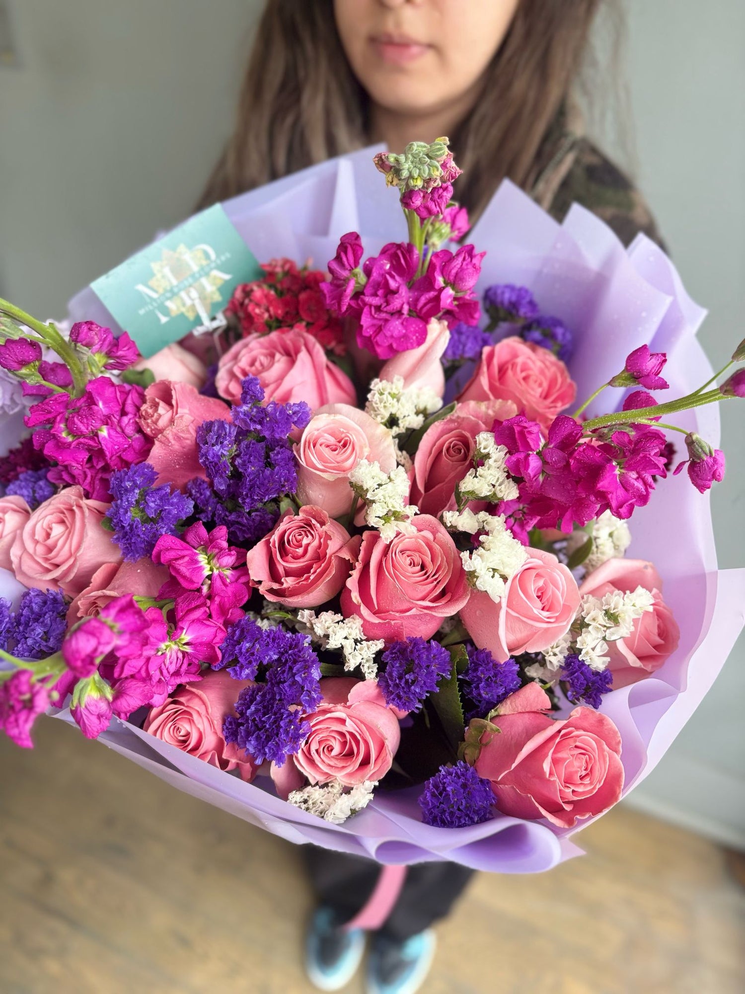 Close-up of a florist’s hands tying a ribbon around a vibrant bouquet of roses, lilies, and baby's breath.