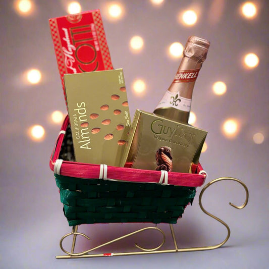 A festive sleigh-shaped gift basket with green and red woven accents, featuring Highland Almond Biscotti, Guylian Belgian chocolates, and other gourmet treats. This holiday basket is perfect for Christmas, seasonal celebrations, and corporate gifting, offering a luxurious assortment of sweets to spread festive cheer.