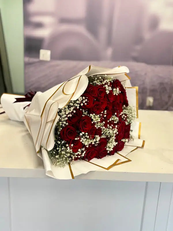 Bouquet of red roses with greenery on a white surface, with a blurred background