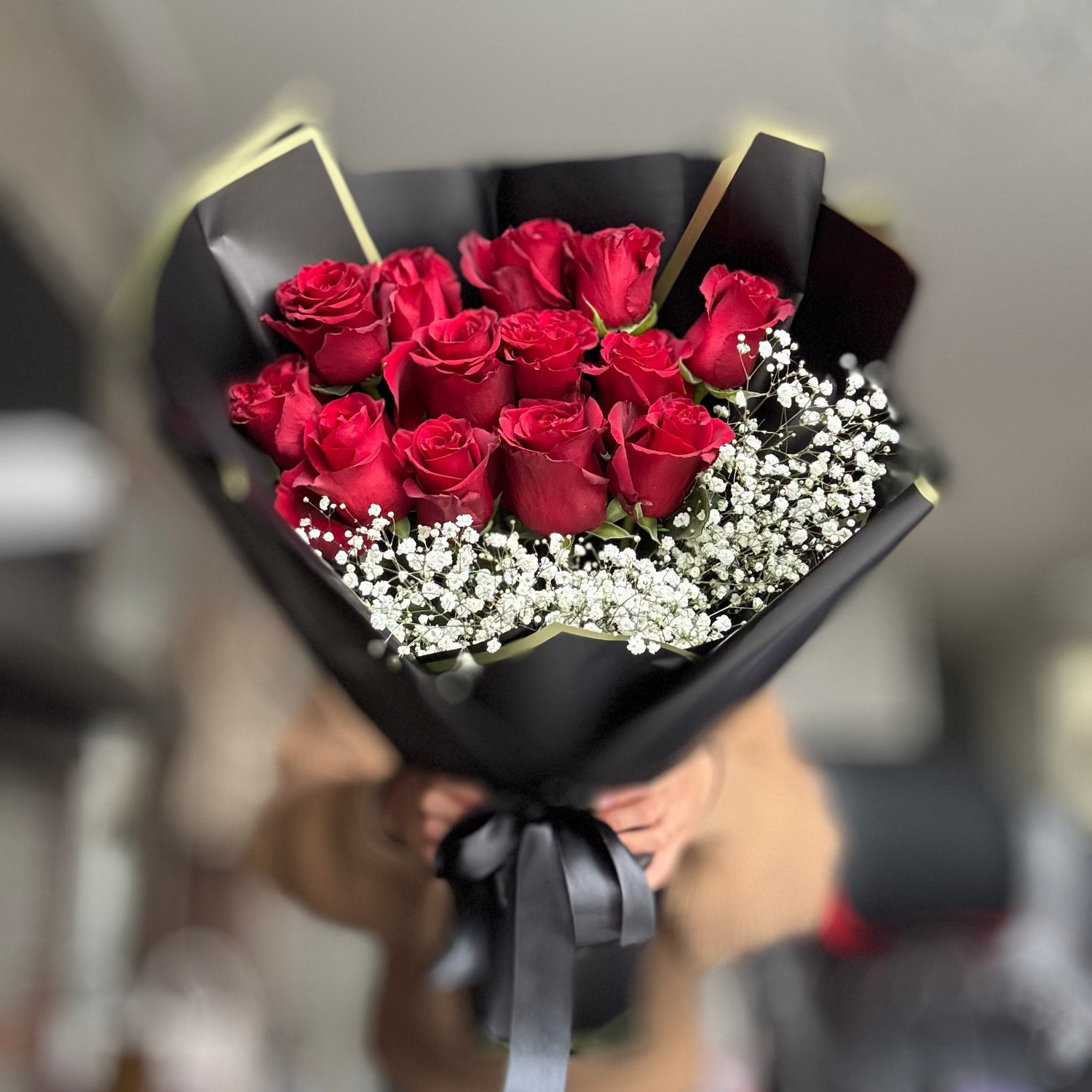 Bouquet of red roses with white flowers wrapped in black paper held by a person.