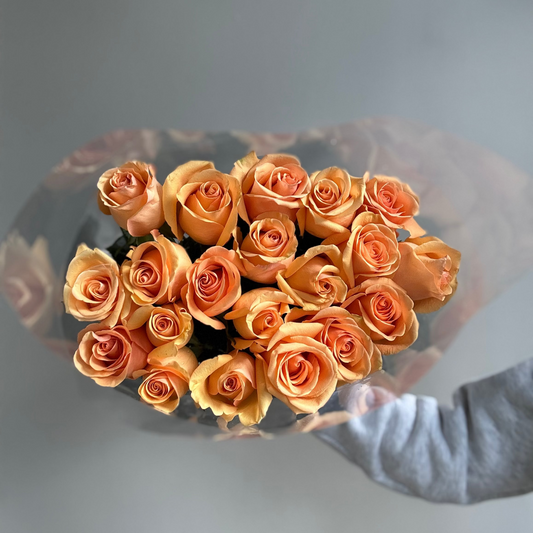 Bouquet of orange roses held by a person against a gray background