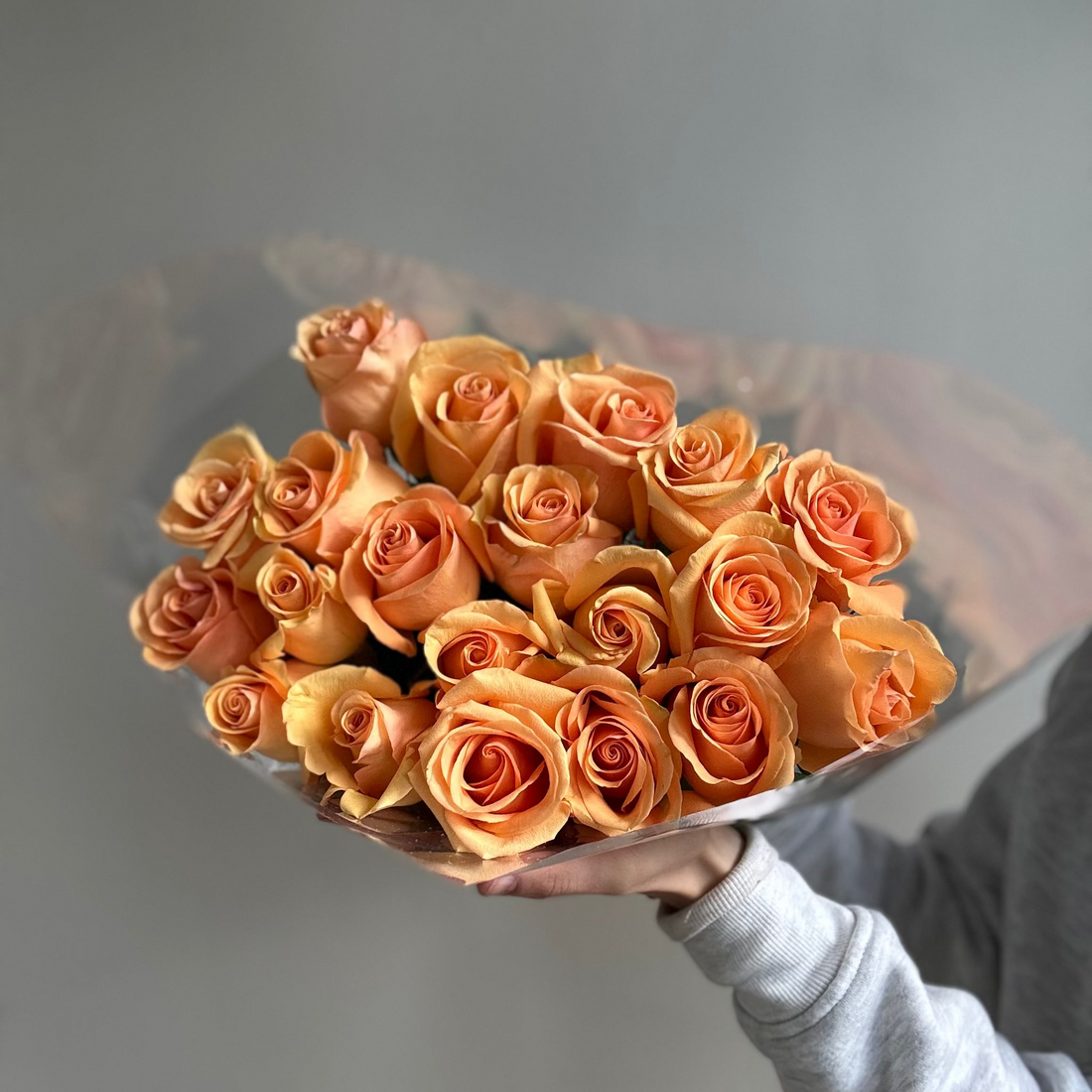 Bouquet of orange roses held by a person against a gray background