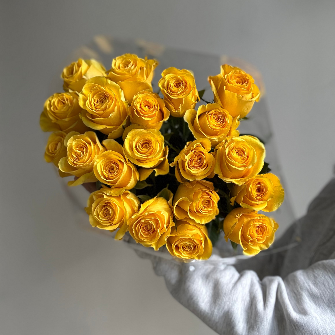 Bouquet of yellow roses in a clear vase on a light gray background