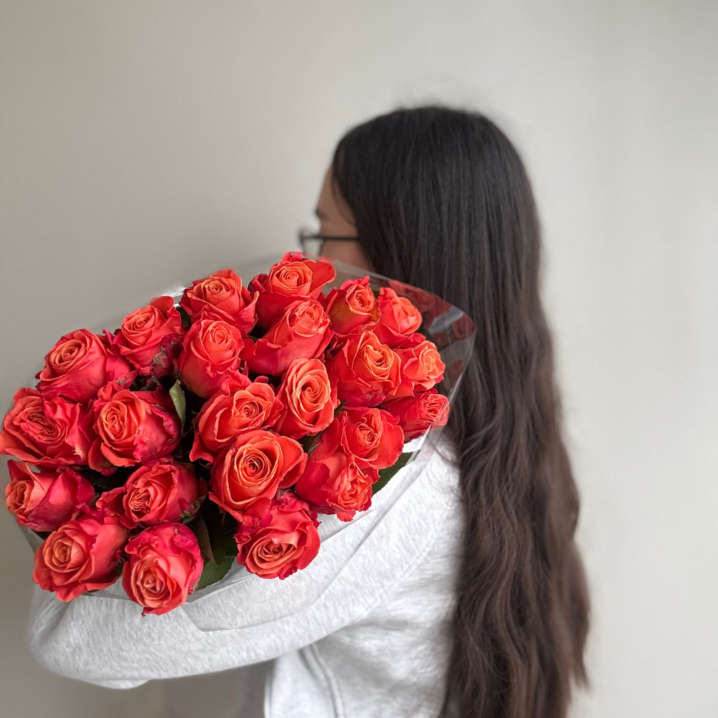 Person holding a large bouquet of red roses against a plain background
