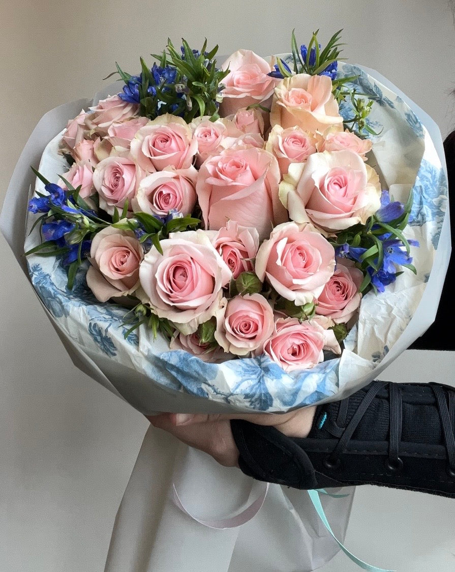 Bouquet of pink roses with blue accents in a decorative wrap on a white background