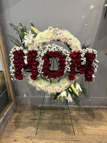 Floral arrangement with 'Mom' in red and white flowers on a stand.