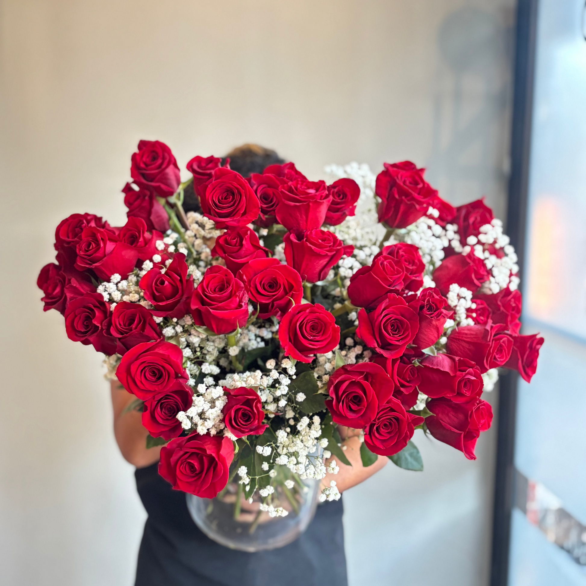 Person holding a large bouquet of red roses with white berries indoors.