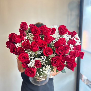 Person holding a large bouquet of red roses with white berries indoors.