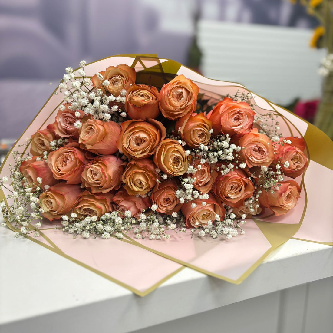 Bouquet of orange roses with a geometric pink and gold wrap on a white surface.