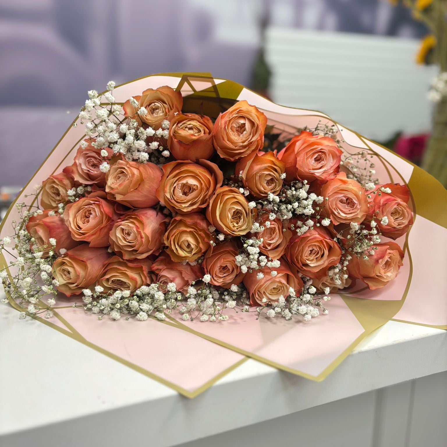 Bouquet of orange roses with a geometric pink and gold wrap on a white surface.