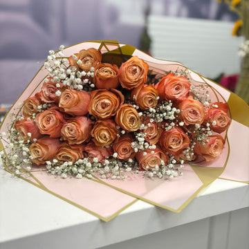Bouquet of orange roses with a geometric pink and gold wrap on a white surface.