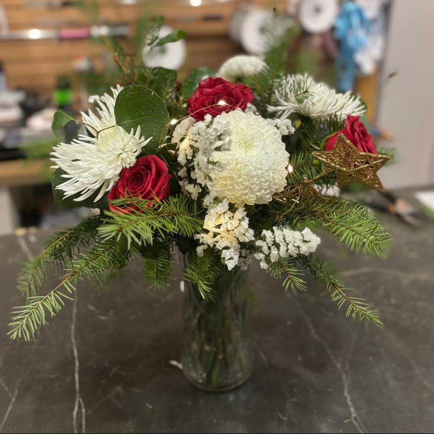 Bouquet of red and white flowers in a clear vase on a dark surface with a blurred background.