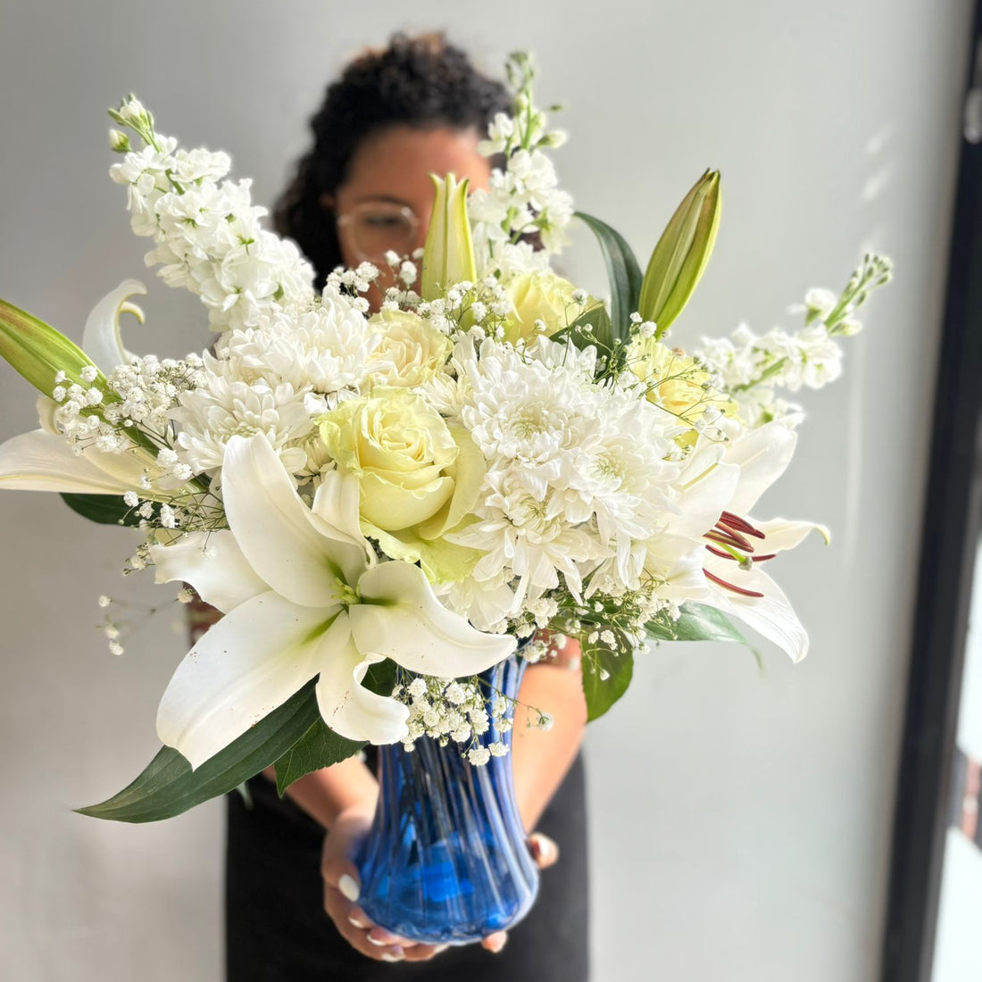 Person holding a bouquet of flowers with a blue vase against a neutral background
