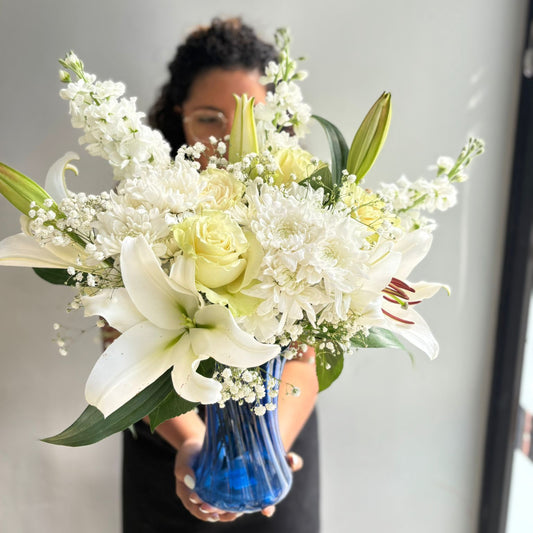 Person holding a bouquet of flowers with a blue vase against a neutral background
