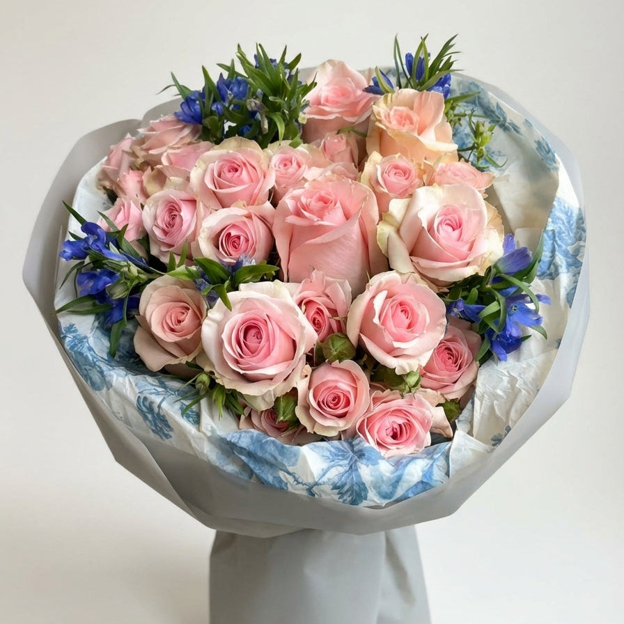 Bouquet of pink roses with blue accents in a decorative wrap on a white background