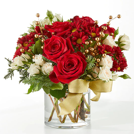 Festive sleigh Christmas floral arrangement featuring vibrant red roses, carnations, cream spray roses, hypericum berries, golden accents, and fresh greenery, arranged in a decorative white sleigh with gold snowflake details. Perfect for holiday decor or gifting