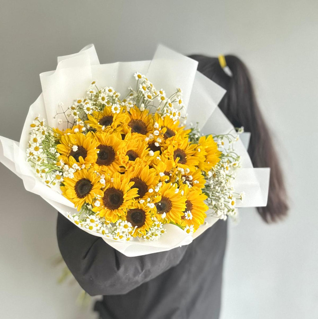 Bouquet of yellow sunflowers and white flowers held by a person wearing a dark coat.