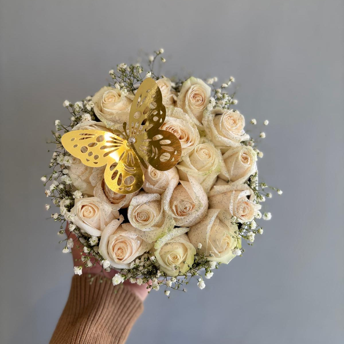 Bouquet of white roses with gold butterflies held by a person against a gray background