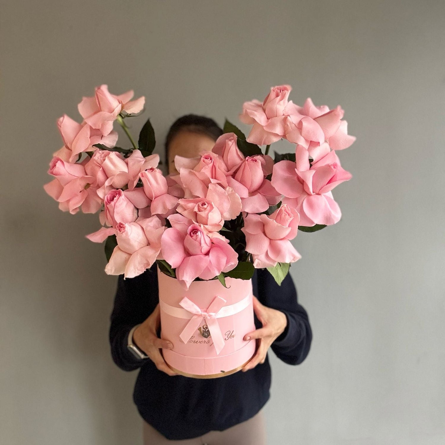 Person holding a large bouquet of pink flowers in a pink container against a plain background