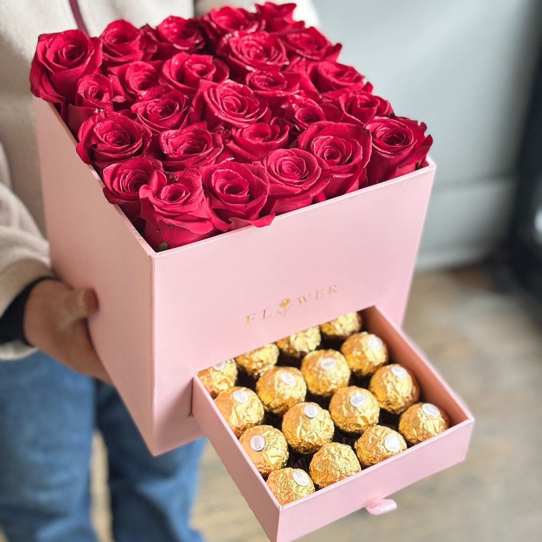 Pink box with red roses and gold Ferrero Rocher chocolates held by a person.