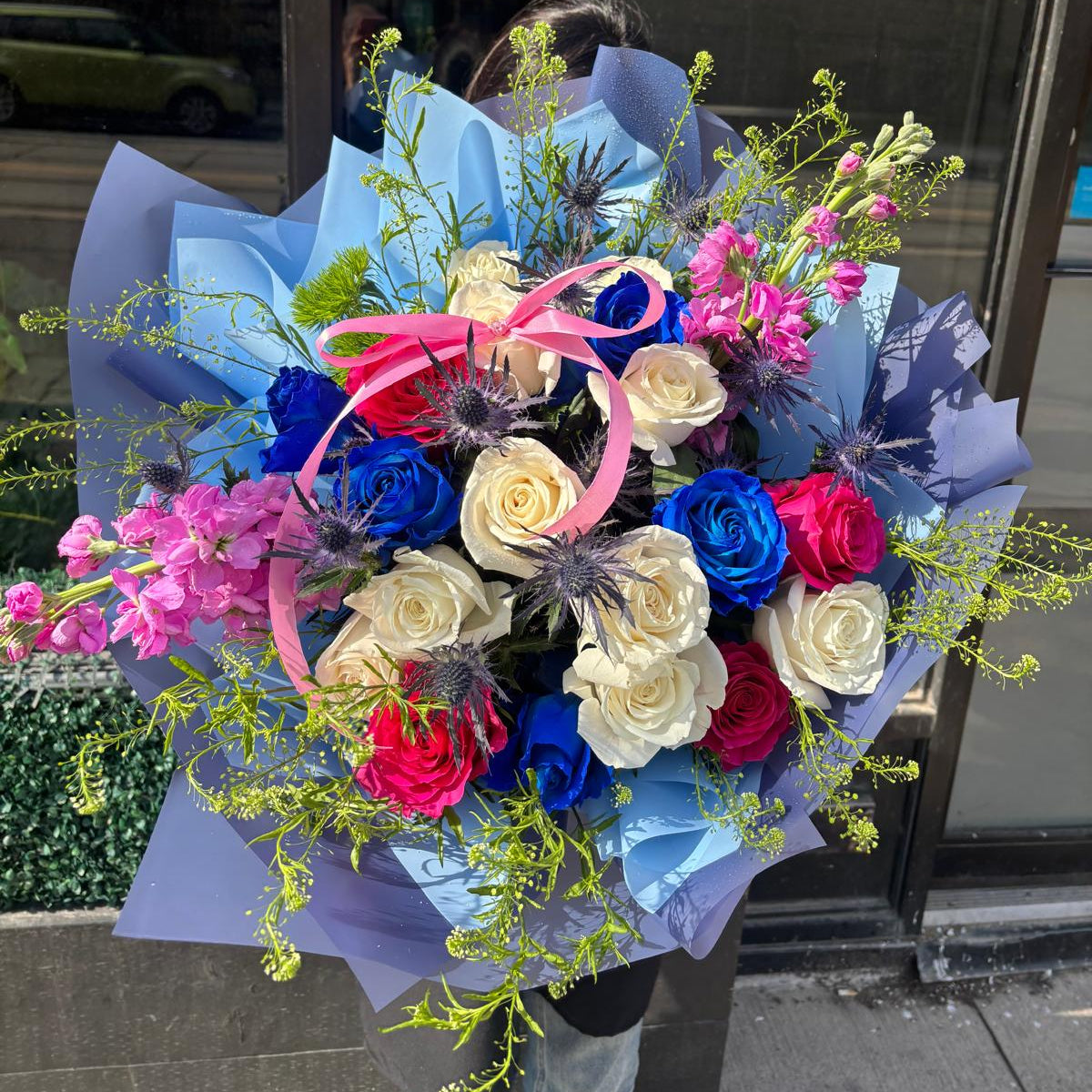 Colorful bouquet of flowers with blue, pink, and red tones against a reflective glass door background.