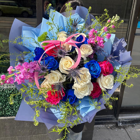 Colorful bouquet of flowers with blue, pink, and red tones against a reflective glass door background.